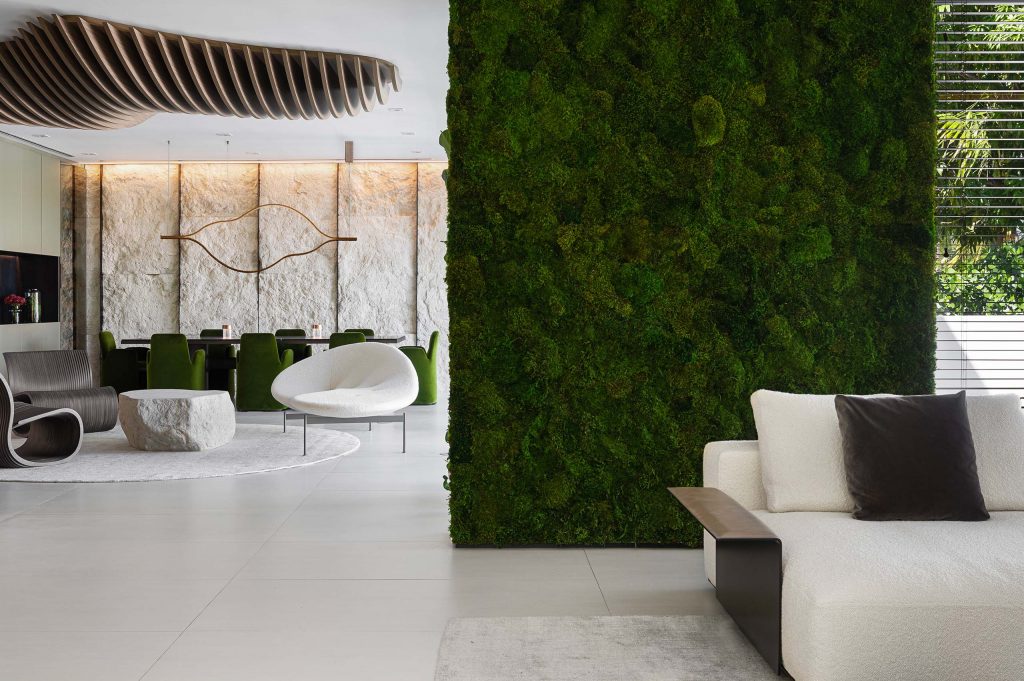 nature inspired design with large moss wall, white sofa and organic shaped furniture, wood ceiling sculpture, rough stone dining wall, and velvet green dining chairs