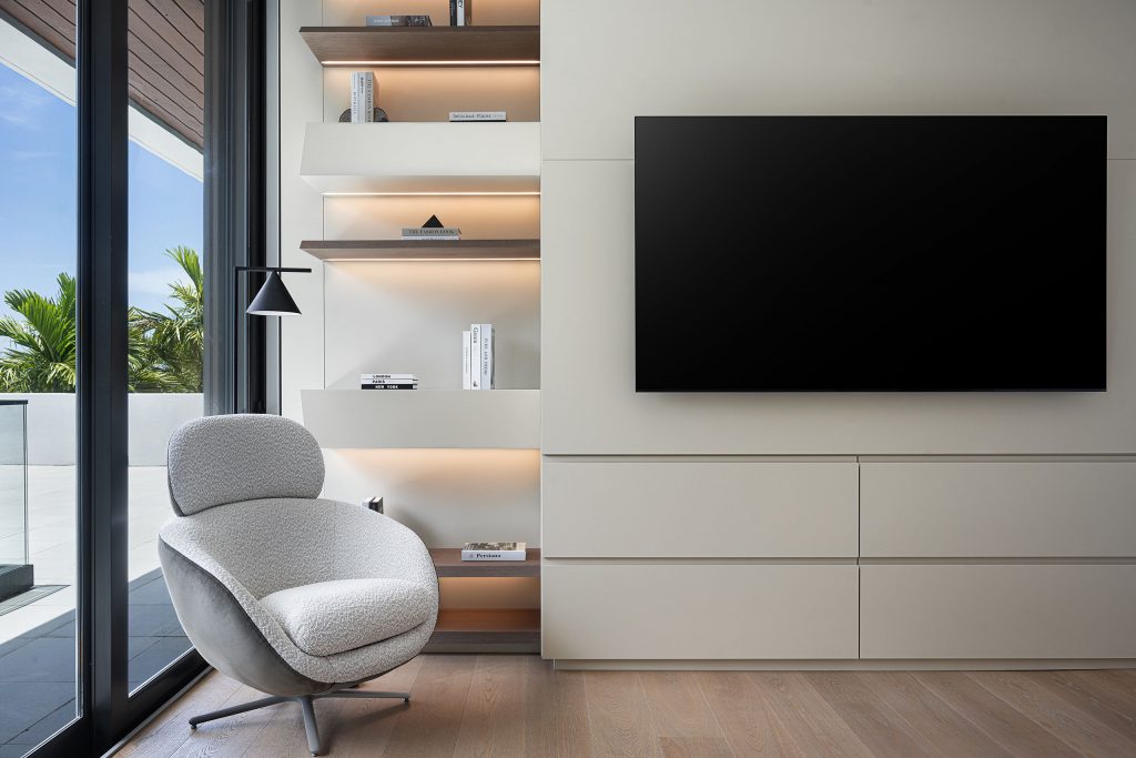 Bedroom Tv wall custom woodwork in sand color, irregular shelves with led illumination, white boucle lounge chair, ash wood floor