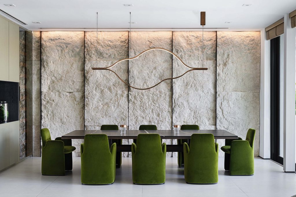 contemporary nature inspired dining room, green velvet dining chairs, black marble dining table, rough stone wall in sand color and metallic bronze wine cellar