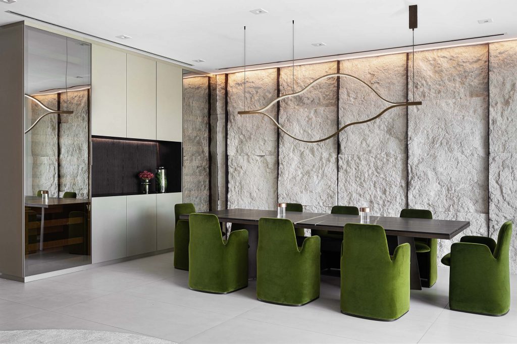 contemporary nature inspired dining room, green velvet dining chairs, black marble dining table, rough stone wall in sand color and metallic bronze wine cellar