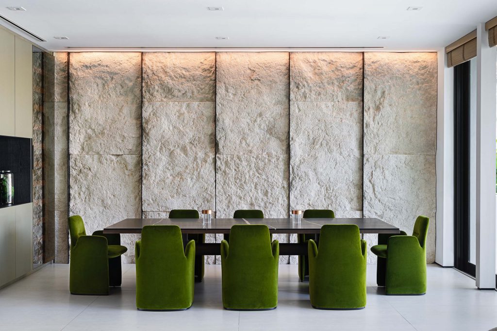 Dining room with textured stone wall, green velvet chairs, and a custom linear pendant in SK Residence