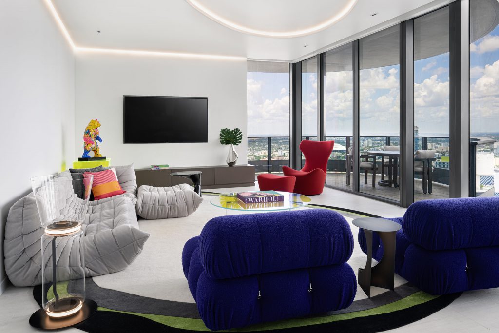 Modern living room with panoramic city view, featuring contemporary furniture and bold colors.