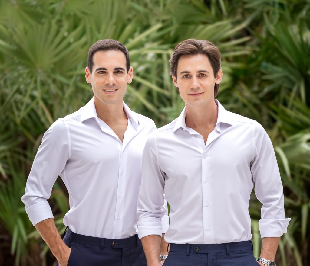 Picture of Miami Luxury Interior Designers Nicholas Gennari and Roberto Racy, wearing white shirts, background showing a lush green landscape.