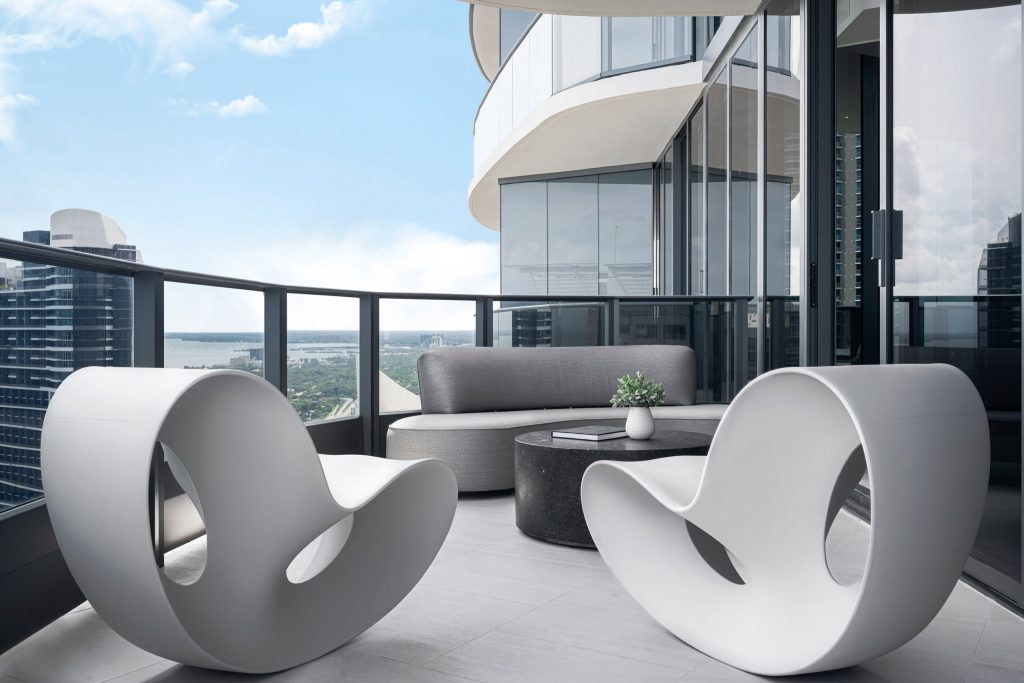 Wraparound terrace with white organic rocking chairs, curved gray sofa, and sweeping Miami skyline views at Brickell Flatiron