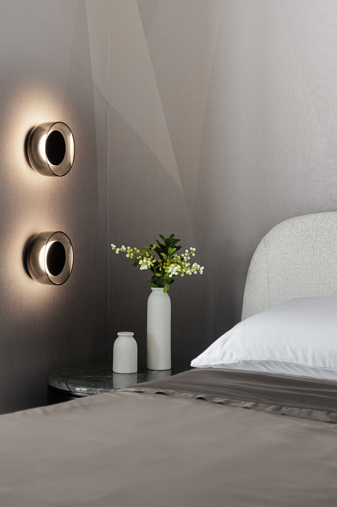 Bedroom detail in FM Apartment with circular wall sconces, green stone nightstand, and upholstered bed.