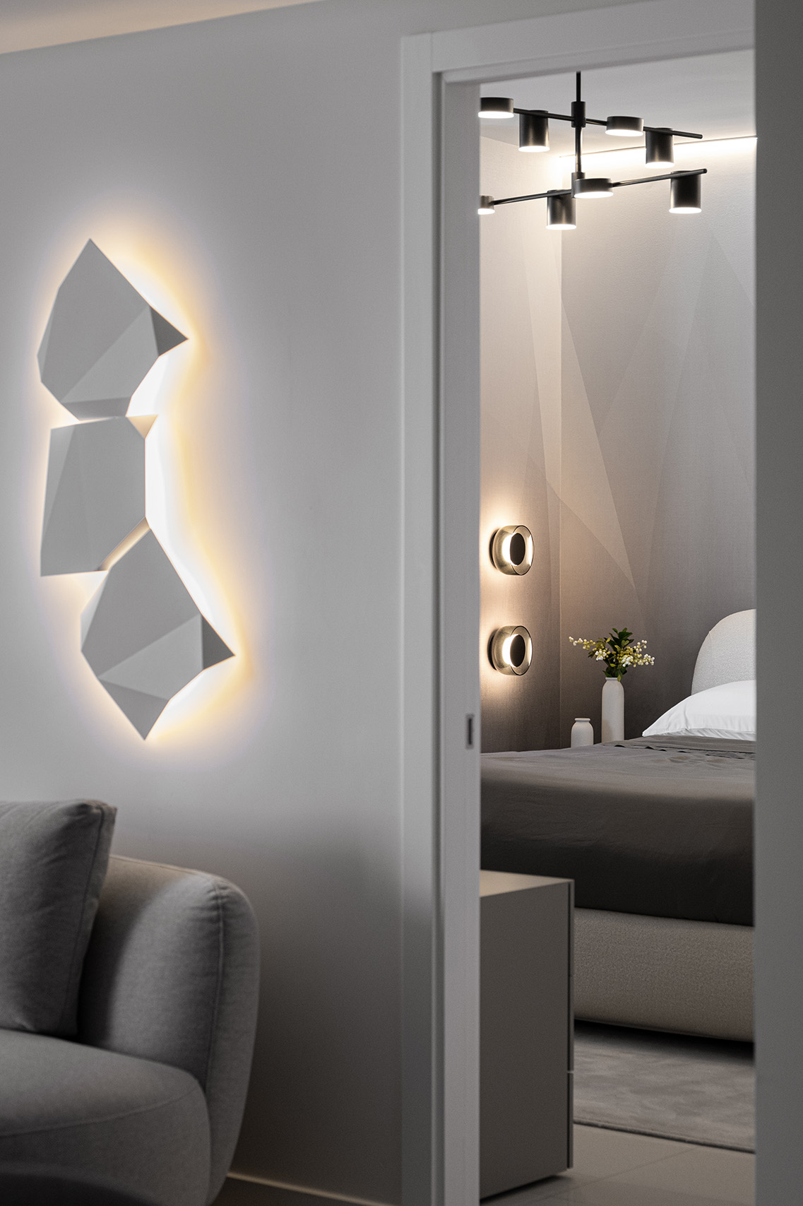 View from the living area into the bedroom in FM Apartment with illuminated wall art and layered lighting.