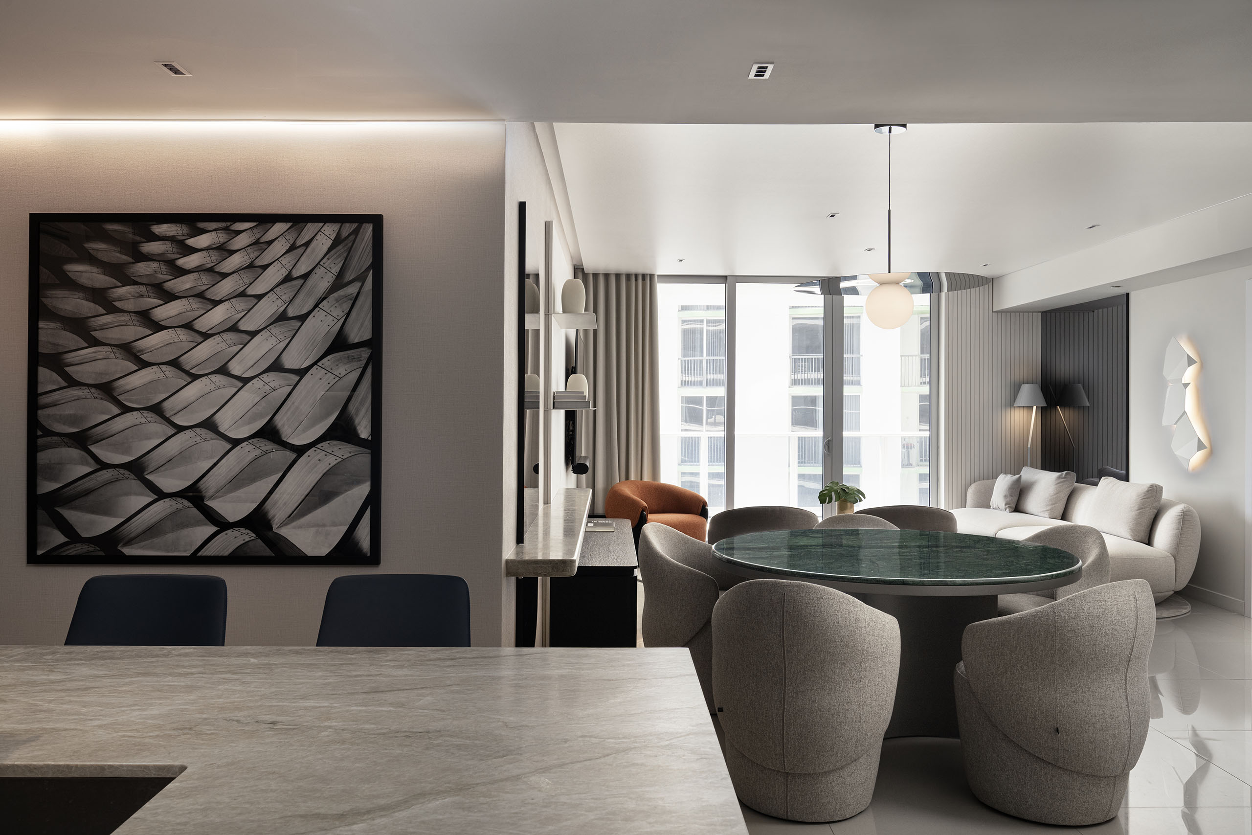 View from the kitchen toward the dining and living area in FM Apartment with curved dining chairs and soft cove lighting.
