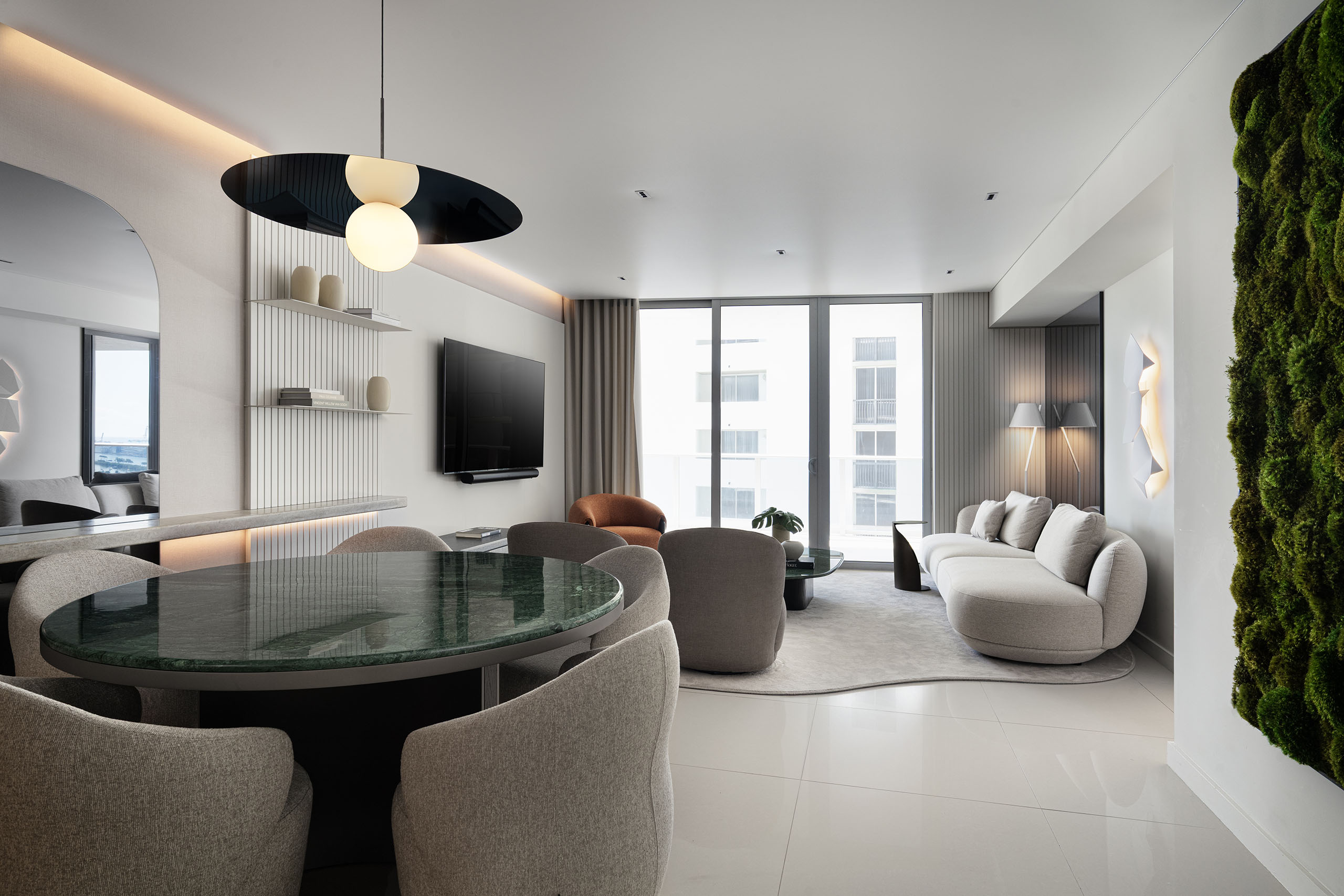 Open-plan living and dining room in FM Apartment at Aria on the Bay with green marble table, curved seating, and moss artwork.