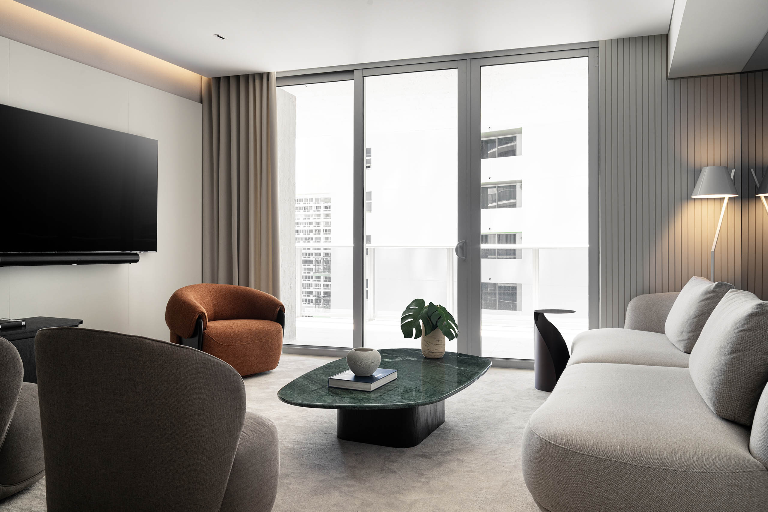 Living room in FM Apartment facing the balcony with curved sofa, rounded lounge chair, and green stone coffee table.