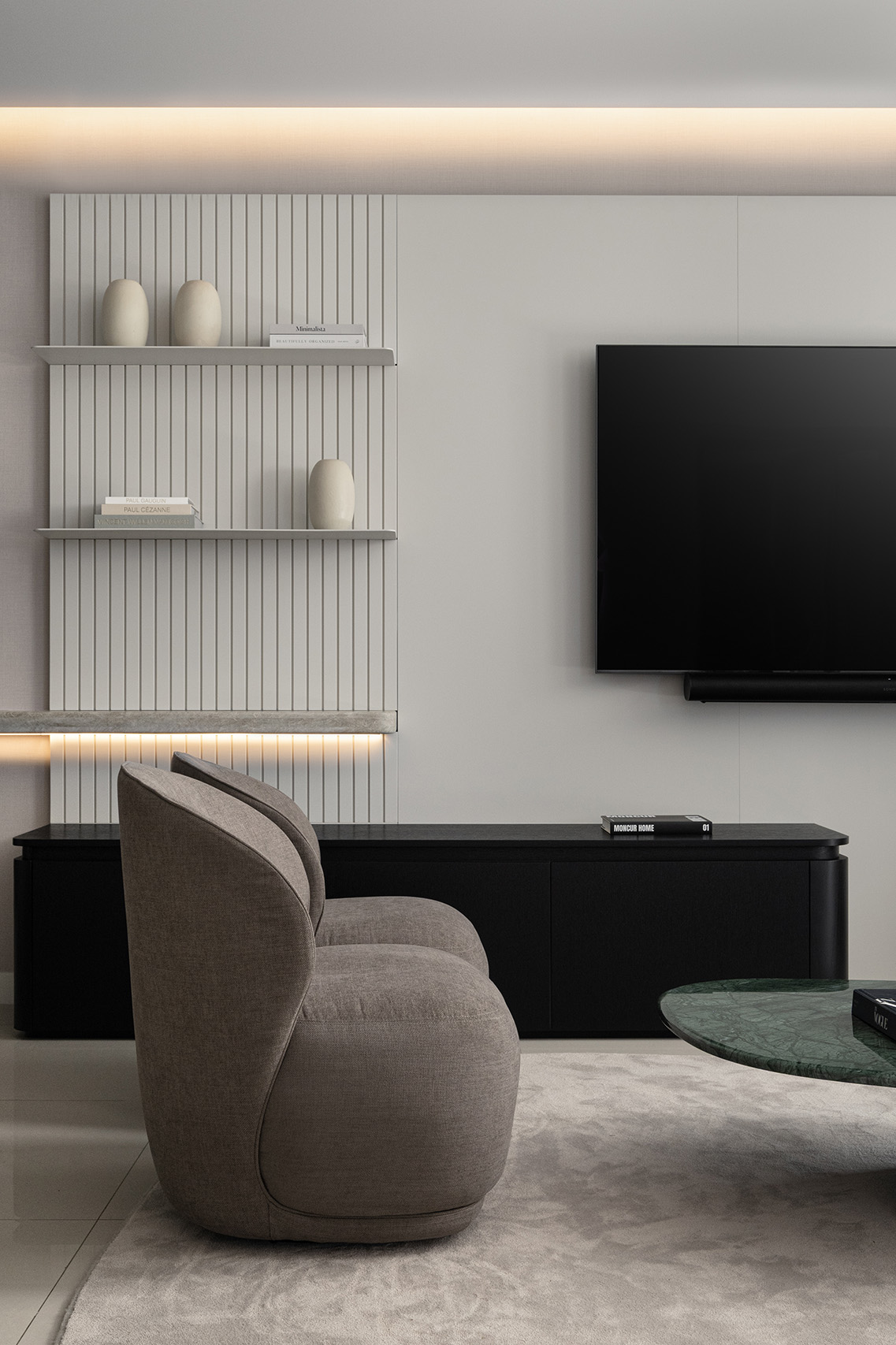 Living room media wall in FM Apartment with fluted paneling, floating shelves, concealed lighting, and lounge chair detail.