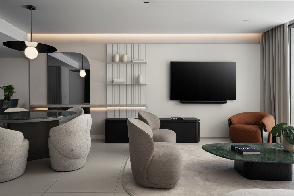 Living room in FM Apartment with integrated media wall, fluted detailing, curved lounge chairs, and green stone coffee table.