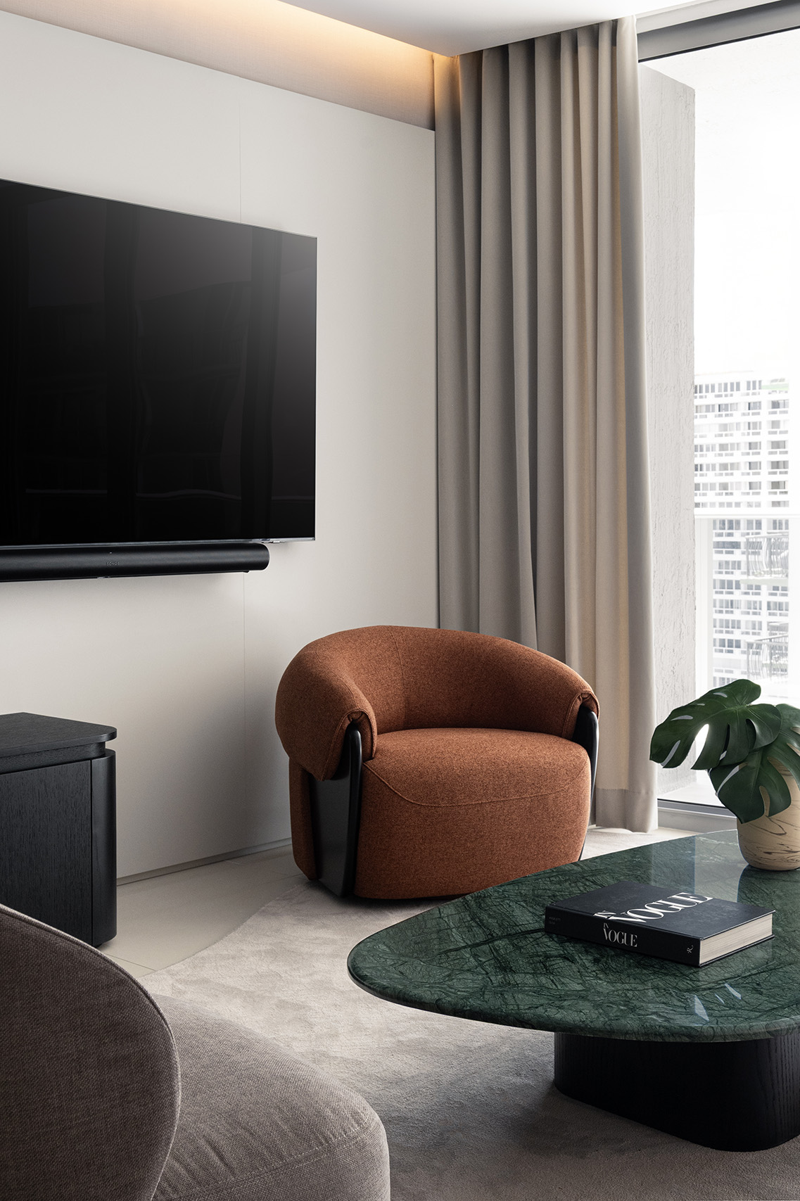 Living room detail in FM Apartment with rust lounge chair, green stone coffee table, and window-side seating area.
