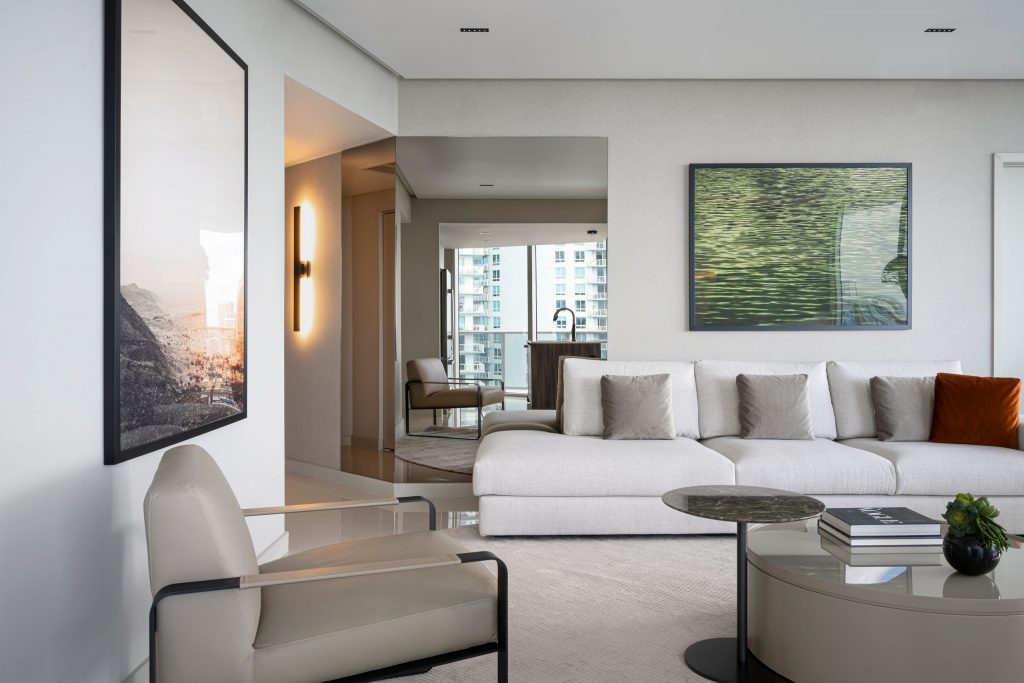 Living room in MB Apartment viewed toward the entry and kitchen with white sofa, armchair, wall sconce, and round tables.