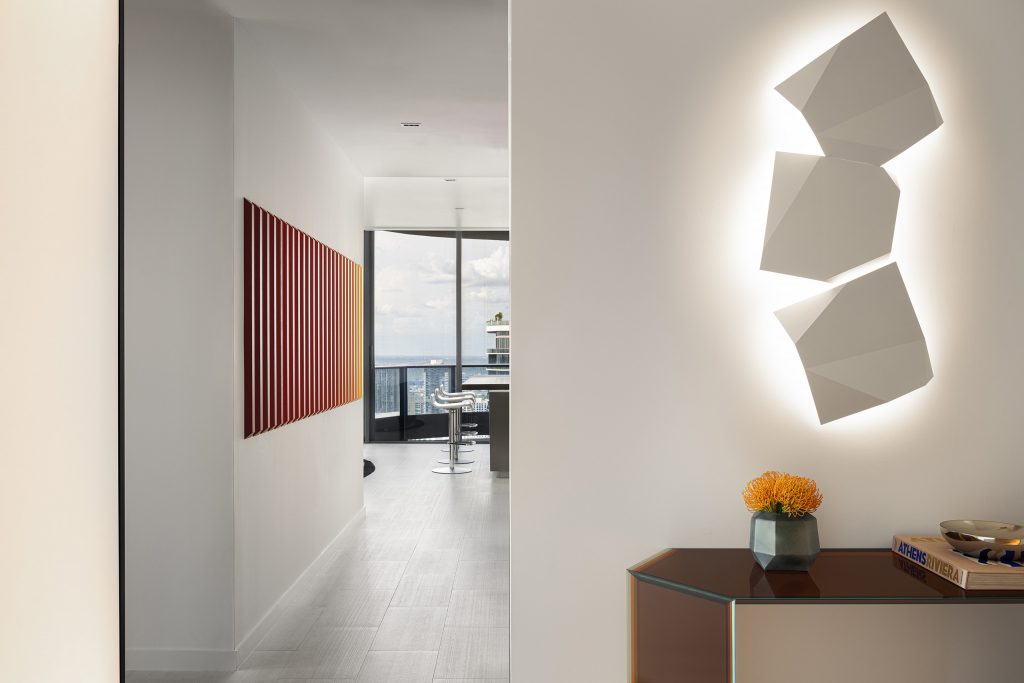 Corridor in JZ Apartment with geometric wall light, red artwork, and a view toward the living area