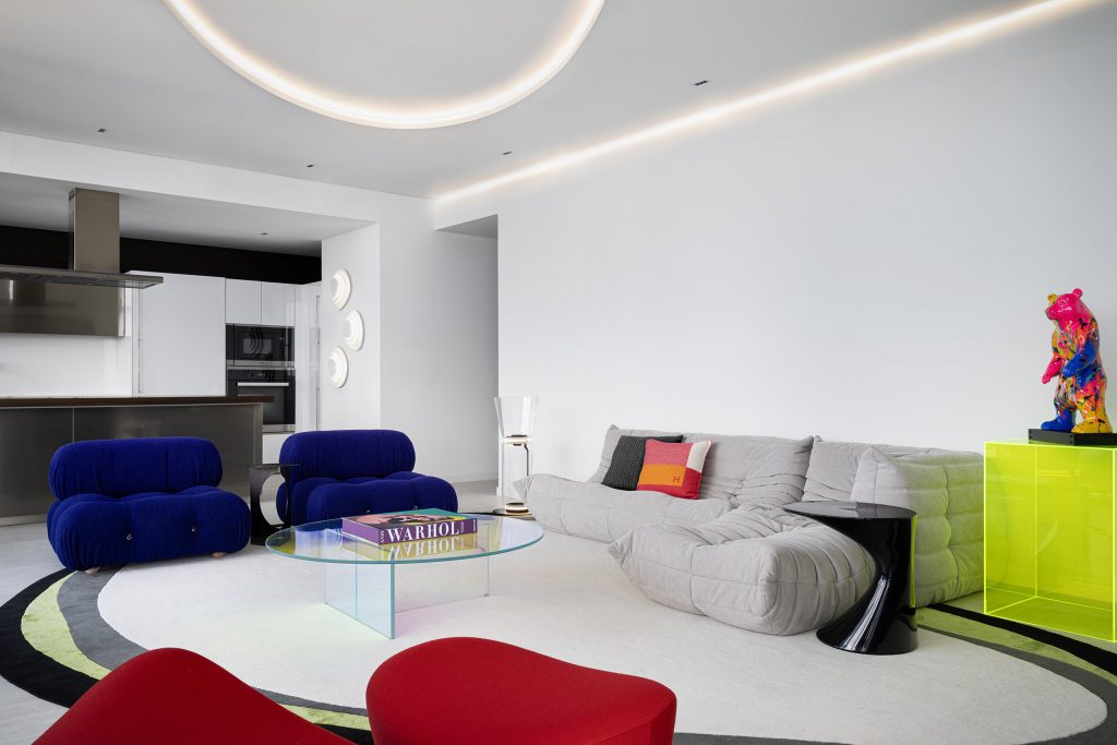 Open living room in JZ Apartment with blue lounge chairs, gray seating, and a view toward the kitchen