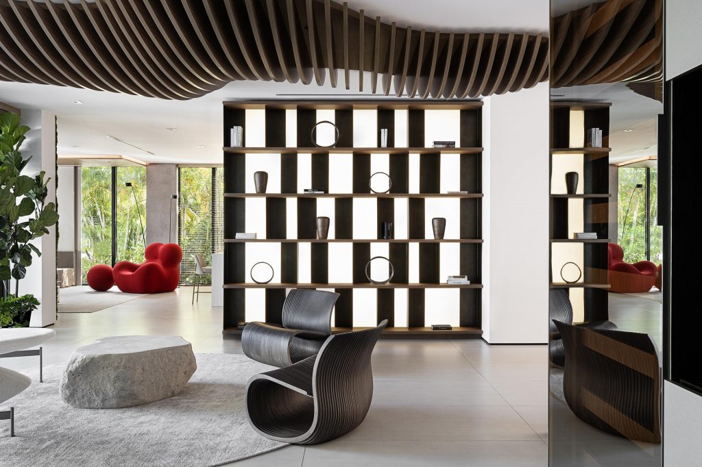 Open lounge with illuminated library wall, sculptural chairs, and a flowing wood ceiling feature