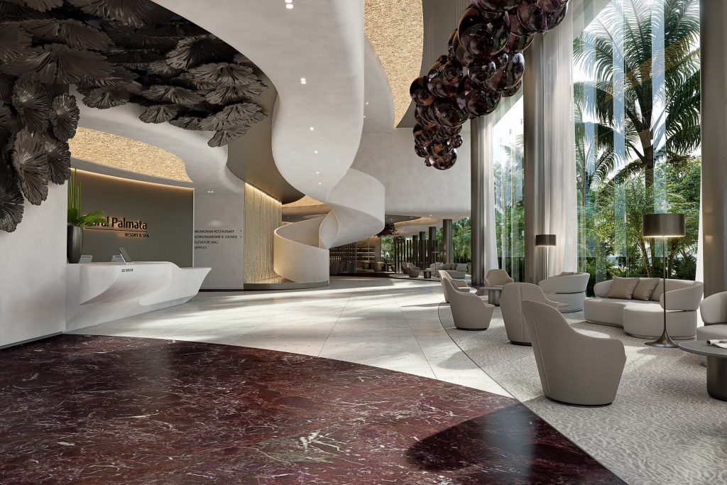 Wide lobby with a sculpted pale stone reception counter on the left beneath a bronze fan coral ceiling installation, a curved white staircase set against a backlit water wall beyond it, and swivel armchairs and curved sofas in cream to the right on a textured rug. Deep burgundy marble is inset into light silver travertine flooring, bronze columns run along floor to ceiling glazing onto palms, and a cluster of mirrored glass spheres in plum hangs in the foreground. The illuminated wall sign reads Coral Palmata Resort & Spa, and the directory beside it lists Meandrina Restaurant, Gorgonian Bar & Lounge, Elevator Hall and Offices.